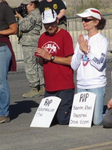 Scott and Claire Schaeffer-Duffy kneel and pray in the road leading into Creech drone base, photo by Felice Cohen-Joppa