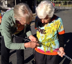 Anneke Corbett assists Frances Crowe in locking her chain to the Vermont Yankee gate. Photo by Marcia Gagliardi
