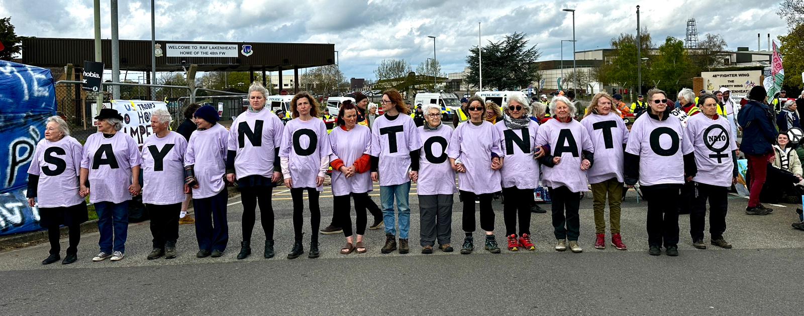 A line of people hold up individual white letters spelling "SAY NO TO NATO" across a street.